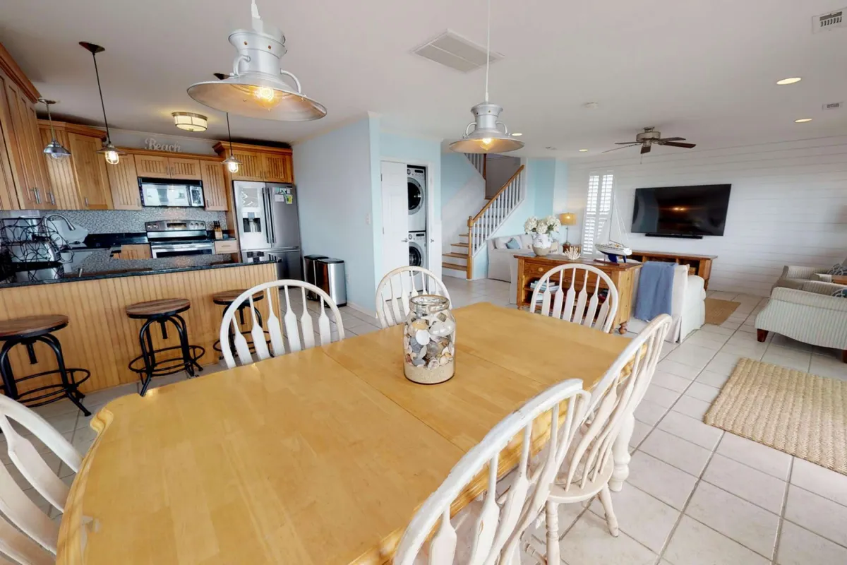 An open-plan interior highlighting a large dining table, kitchen island, and cozy living area with a TV. The arrangement is perfect for gathering, entertaining, and sharing meals, with an inviting and homey atmosphere.