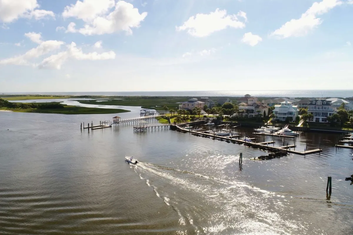 A serene waterfront scene featuring a waterway with a marina, docked boats, and houses lining the shore. The area is peaceful, ideal for boating, water sports, and experiencing coastal life beyond the beach.