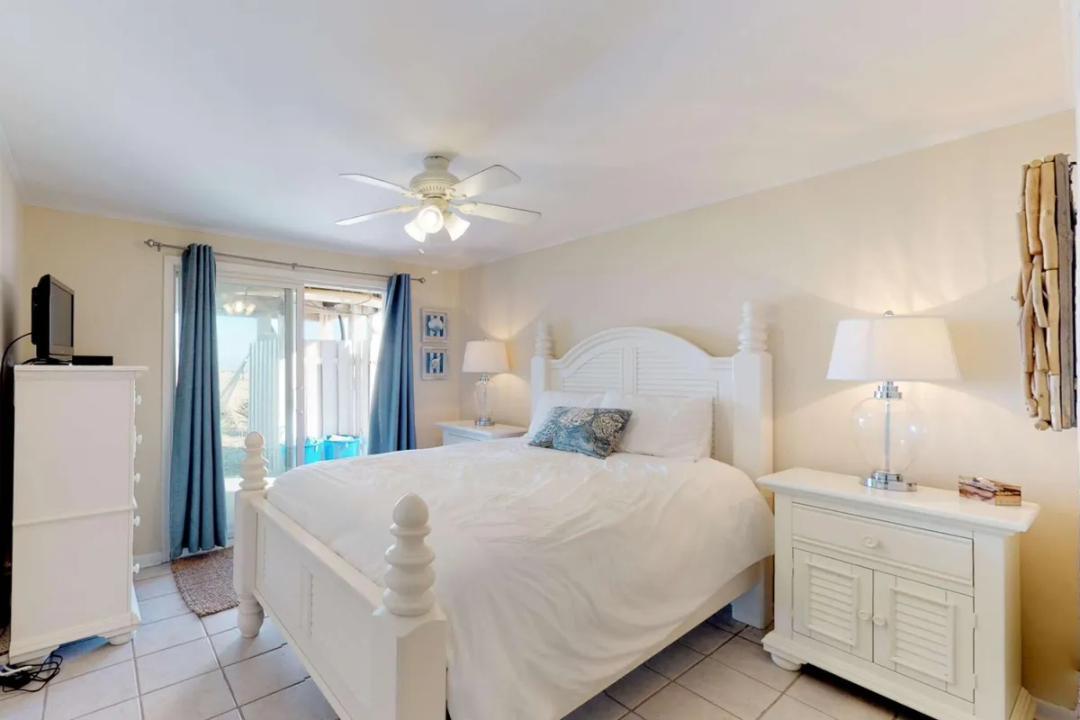 A serene bedroom scene featuring a large, inviting bed with plush linens, flanked by nightstands and softened by gentle sunlight filtering through curtains. The dresser and reading lamp complete a tranquil retreat perfect for decompressing after a day of adventure.