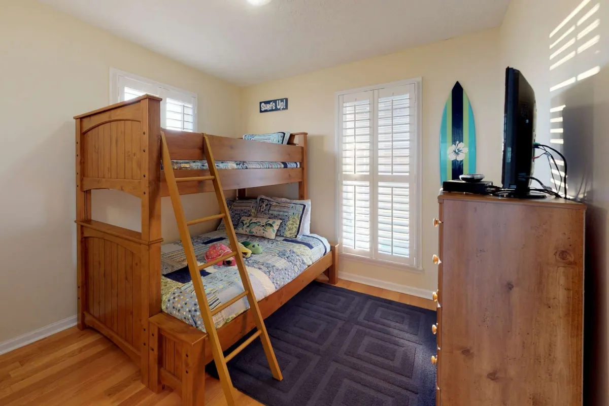 A bright, inviting bedroom featuring a bunk bed, surfboard, television, and soft, draped bedding. The space feels playful yet organized, providing both a fun retreat and plenty of comfort for younger guests.