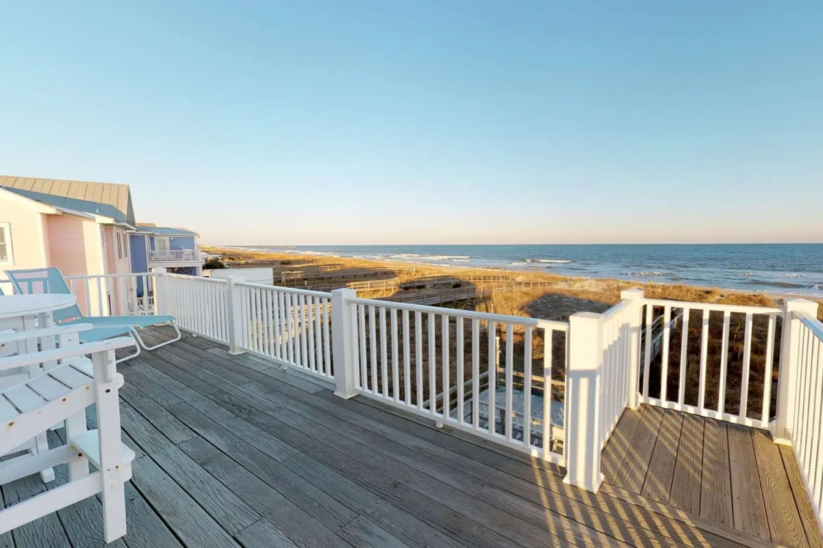 An oceanfront deck furnished with comfortable chairs overlooking the water, surrounded by sturdy railings. The view invites guests to gather for sunset watching, group meals, or stargazing in the evening sea breeze.
